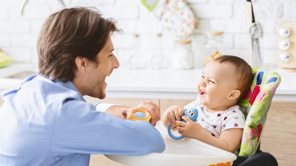 Obraz premium Millennial man laughing with his baby son in kitchen
