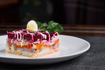 Herring salad under a fur coat with crabs on a white plate. Layered salad with herring, beets, carrots, onions, potatoes and eggs.