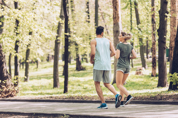 young man in woman in sportswear talking while jogging in green park