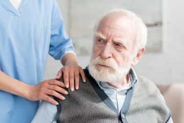 Nurse putting hands on shoulder of sad grey haired man