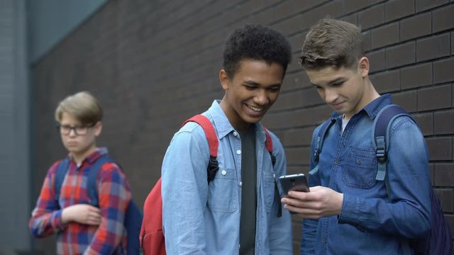 Two bully boys posting offensive video about upset guy behind, cyberbullying