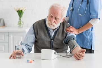 Nurse measuring blood pressure of calm grey haired man
