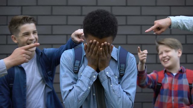 Mean teenagers pointing fingers at black boy crying, verbal bullying, bad rumors