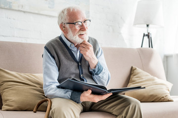 Happy grey haired man holding photo album, looking away