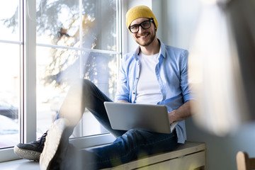 Young businessman working on modern loft office. Man sitting by the window, using contemporary...