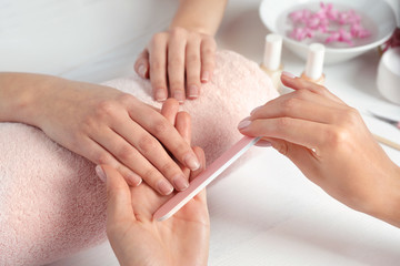 Manicurist filing client's nails at table, closeup. Spa treatment