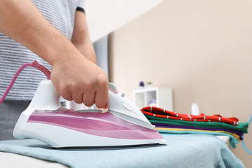 Man ironing clothes on board at home, closeup. Space for text