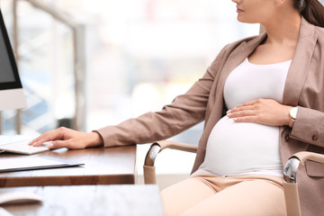 Young pregnant woman working with computer at table in office, closeup
