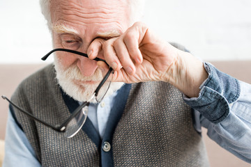 Sad senior man holding glasses, and covering eye of his hand
