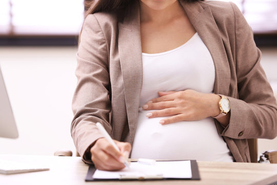 Young pregnant woman working at desk in office, closeup