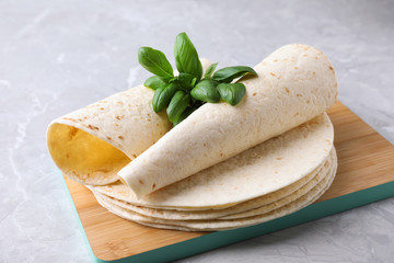 Board of tasty tortillas with basil leaves on grey table, closeup