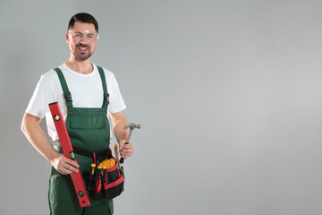 Portrait of professional construction worker with tools on grey background, space for text