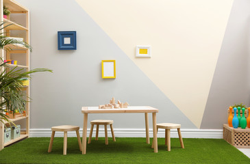Stylish playroom interior with table, stools and green carpet