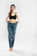 Attractive young woman with slim body wearing her old big jeans on white background. Space for text
