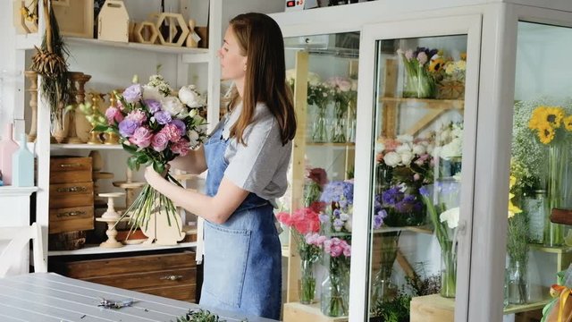Charming young woman florist makes an exclusive bouquet of exquisite flowers in her flower shop. Concept bouquets for events and weddings