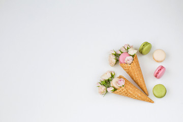 in two wafer cones, pink roses and macarons on white background