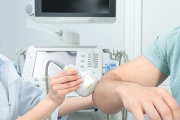 Doctor conducting ultrasound examination of patient's elbow in clinic, closeup
