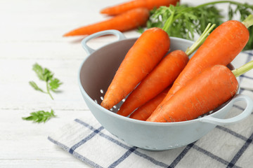 Carrots in colander on white table, closeup