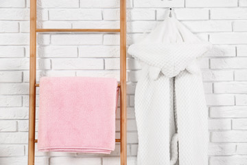 Decorative ladder with clean towel and robe near brick wall