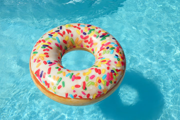 Fototapeta na wymiar Bright inflatable doughnut ring floating in swimming pool on sunny day