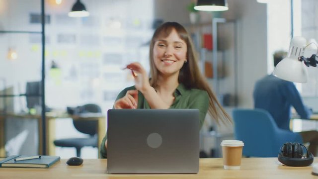 Young Beautiful Brunette Works on a Laptop Computer in Cool Creative Agency in a Loft Office. She is Happy, Smiling, Dancing and is Having Fun.