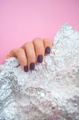 Young woman's hand with beautiful manicure on pink background with metallic shiny paper.