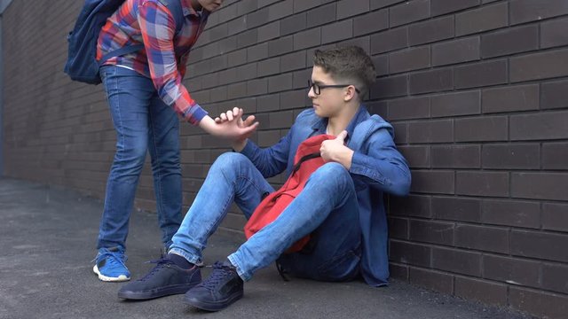 Kind teenage student giving helping hand to bullied nerd boy, supportive friend