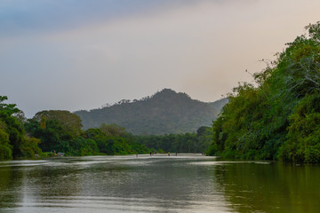 A wide, shallow river flows calmly through the deep South American jungle at blue violet dusk