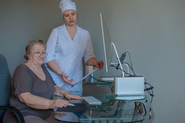 Rather an elderly woman received social assistance for new computer of last modification.  pensioner can order medicines and products online. Nurse in white coat helps woman to master computer.
