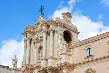 Fototapeta na wymiar Detail of beautiful Syracuse Cathedral on Piazza Duomo Square with blue sky. Baroque architecture, medieval sculptures. Religious temple. Cross. Taken in Ortigia Island, Syracuse, Sicily, Italy