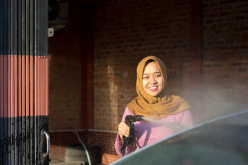 portrait of happy hijab women car cleaning - Removing the soap with water, using a garden hose and a spray gun.