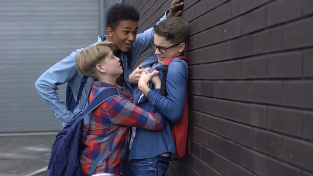 Cruel teenage students bullying nerd boy in school backyard, social problem