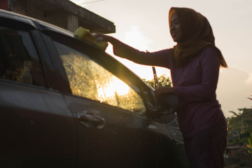 hijab Woman car washing with yellow sponge  washing her car  in front of the house