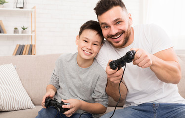 Happy boy enjoying video game with his daddy, playing with joysticks