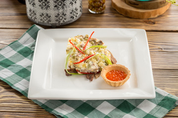 Traditional Russian salad Olivier with red caviar on square plate on wooden table