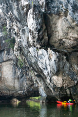 Kayaking through large steep limestone cliff in the sea.