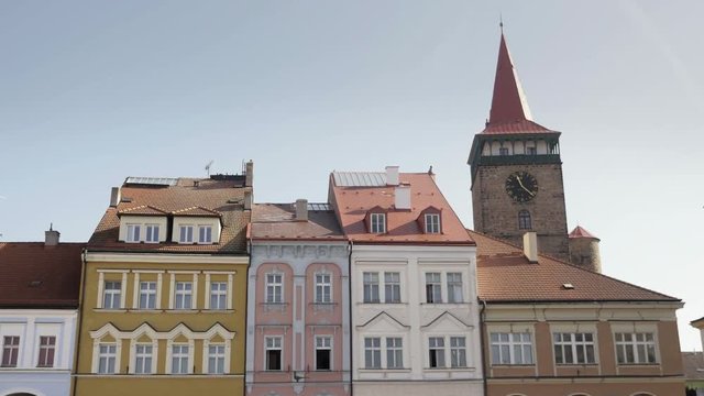 Medieval Renaissance square with stone tower and clock. View to row of houses with colorful old facades and blue sky. Age-old gas lamp and arcades. Static sunny day shot, color corrected footage