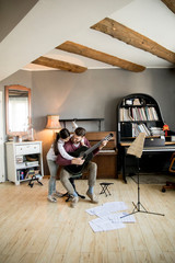 Cute little girl and her handsome father are playing guitar and smiling while sitting  in the room