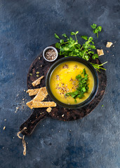 Pumpkin and vegetables cream soup with pumpkin seeds, slices of bread and parsley over a dark background with Space for text. Vegan Food Concept. Hard sunlight, hard shadows, top view.