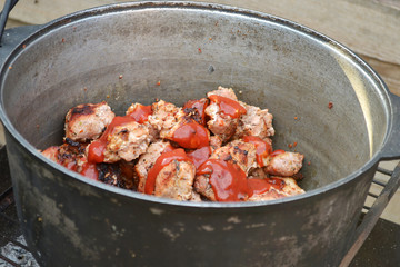 Meat from the grill with ketchup in a pot on the grill, against a wooden fence
