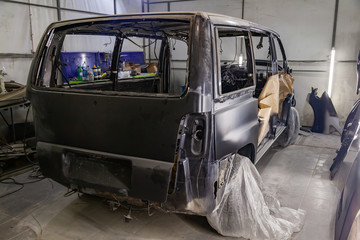 A large black matte car without windows is covered in paper and adhesive tape to protect against splash during painting and repair after an accident in a workshop for body repair of vehicles