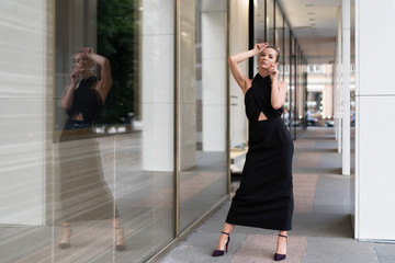 European model originally posing in a black dress near the boutique. In the glass you can see its reflection. Very stylish interesting atmosphere for advertising fashion trends.
