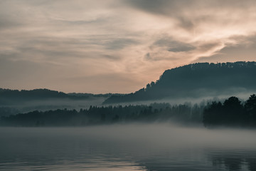Naklejka na ściany i meble landscape with fog over the lake and forest in the evening. evening fog over the lake. 