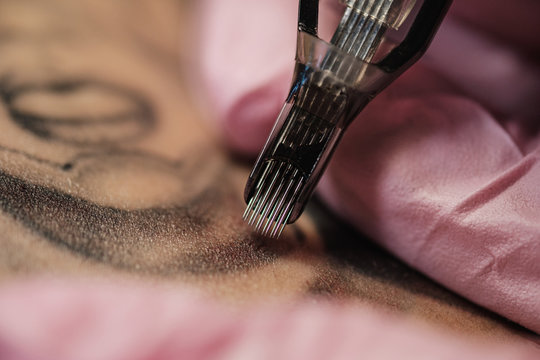 Close-up of a tattoo needle. The process of the tattoo master. Pink women's protective gloves.