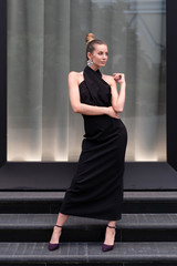 Beautiful girl in a long black dress posing in full growth near the boutique. Graceful interesting poses.