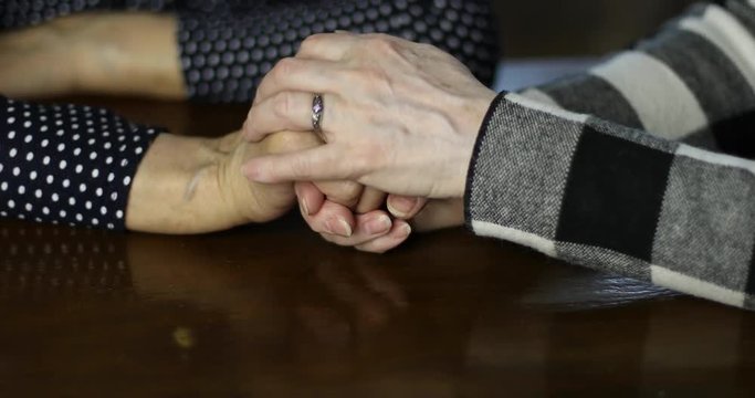Adult hands stroking senior female hands with deep wrinkles.