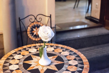 White rose in vase on mosaic table at evening