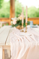 Table for guests, decorated with candles, served with cutlery and crockery and covered with a tablecloth blue plate and golden fork and knife on pink gauze napkin.