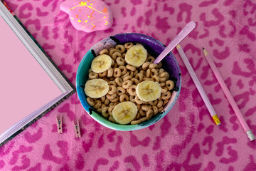 Bowl of cereals with book and pencils over pink animal print background 