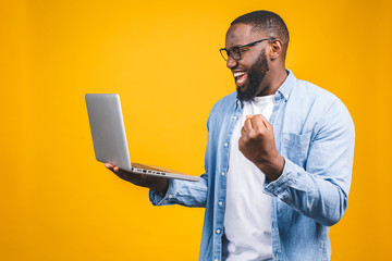 Excited happy afro american man looking at laptop computer screen and celebrating the win isolated over yellow background. - 272866039